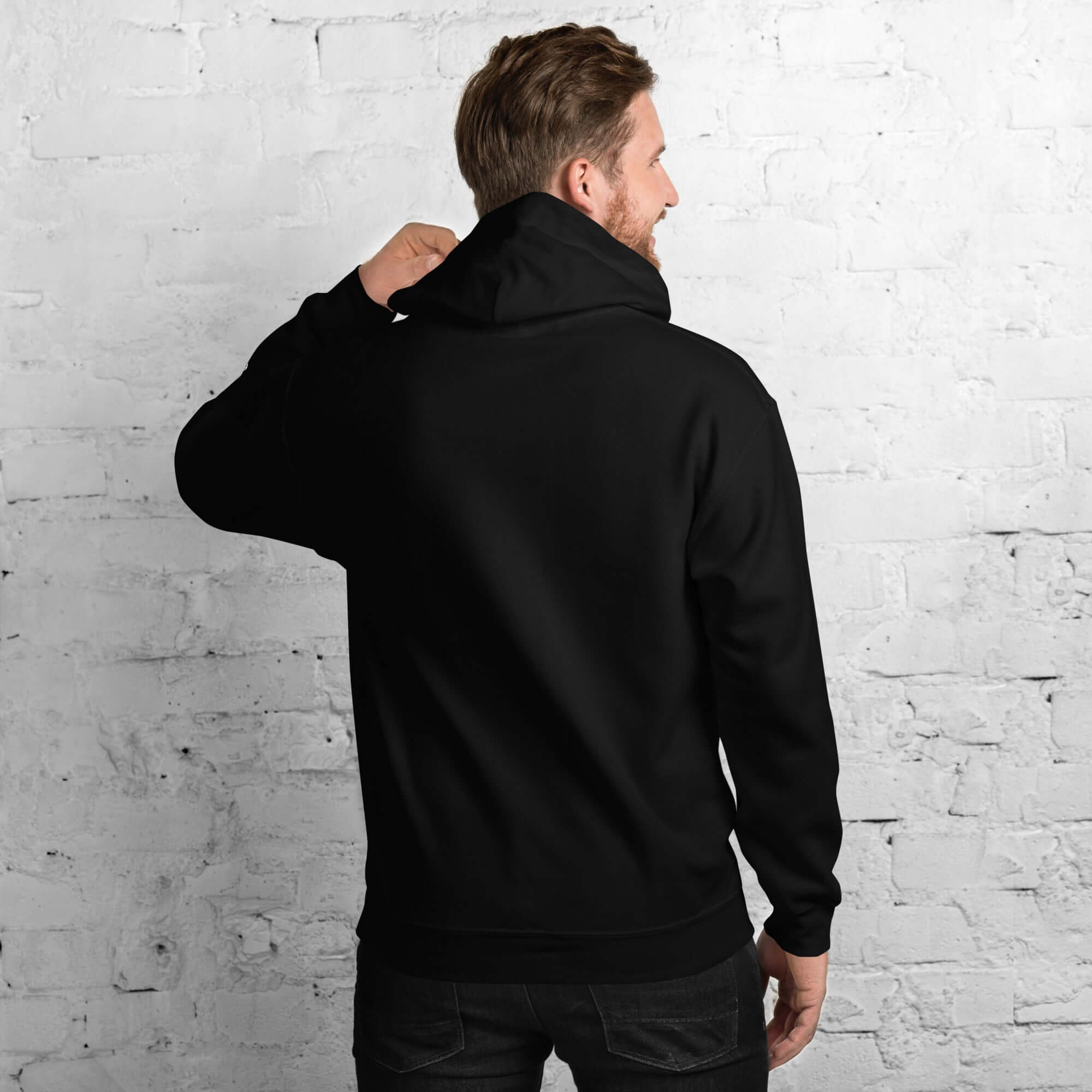Man wearing a black Men’s Hoodie from the Core Collection, showcasing the back view against a brick wall.