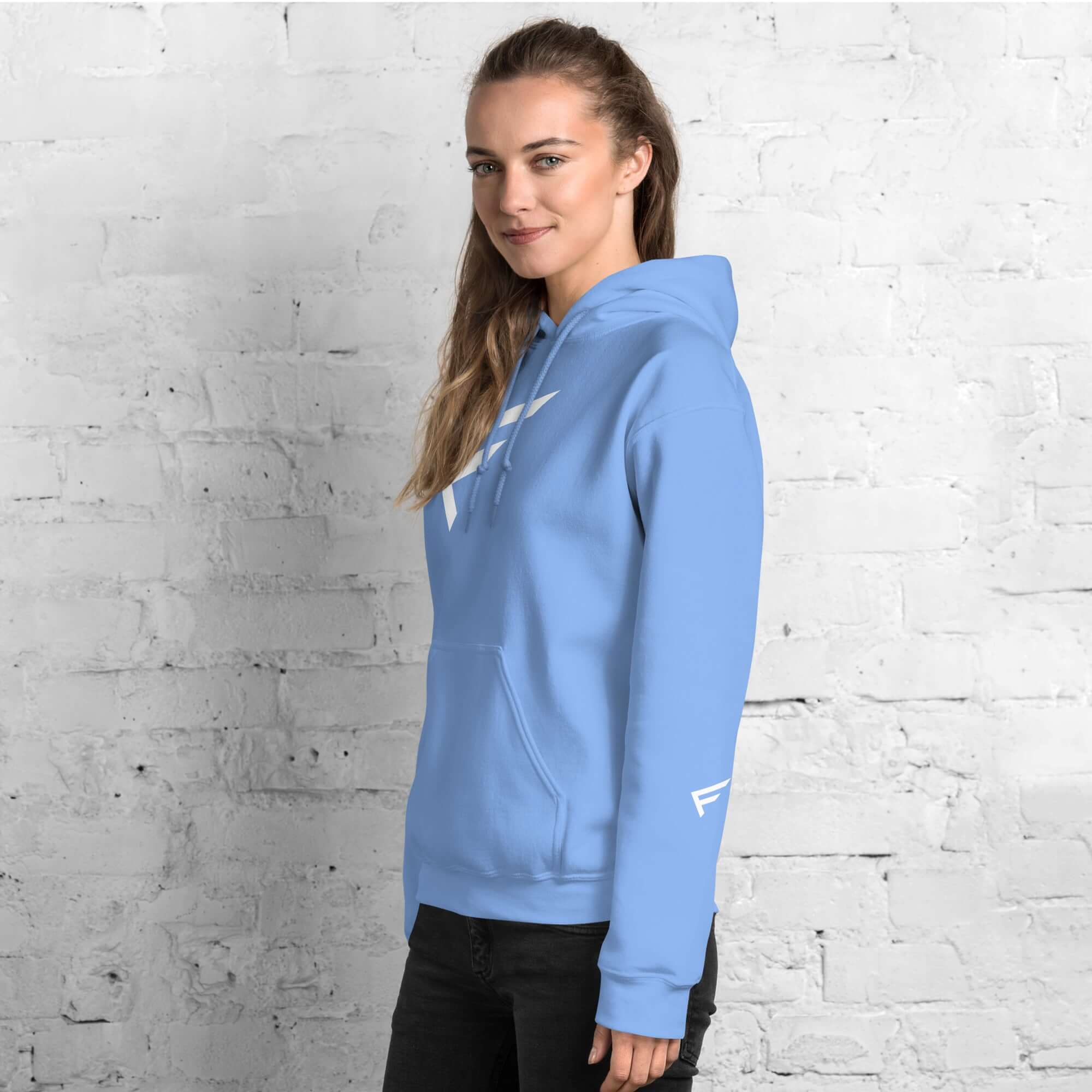 Woman wearing a light blue hoodie with an 'F' emblem, highlighting comfort and style against a white brick background.