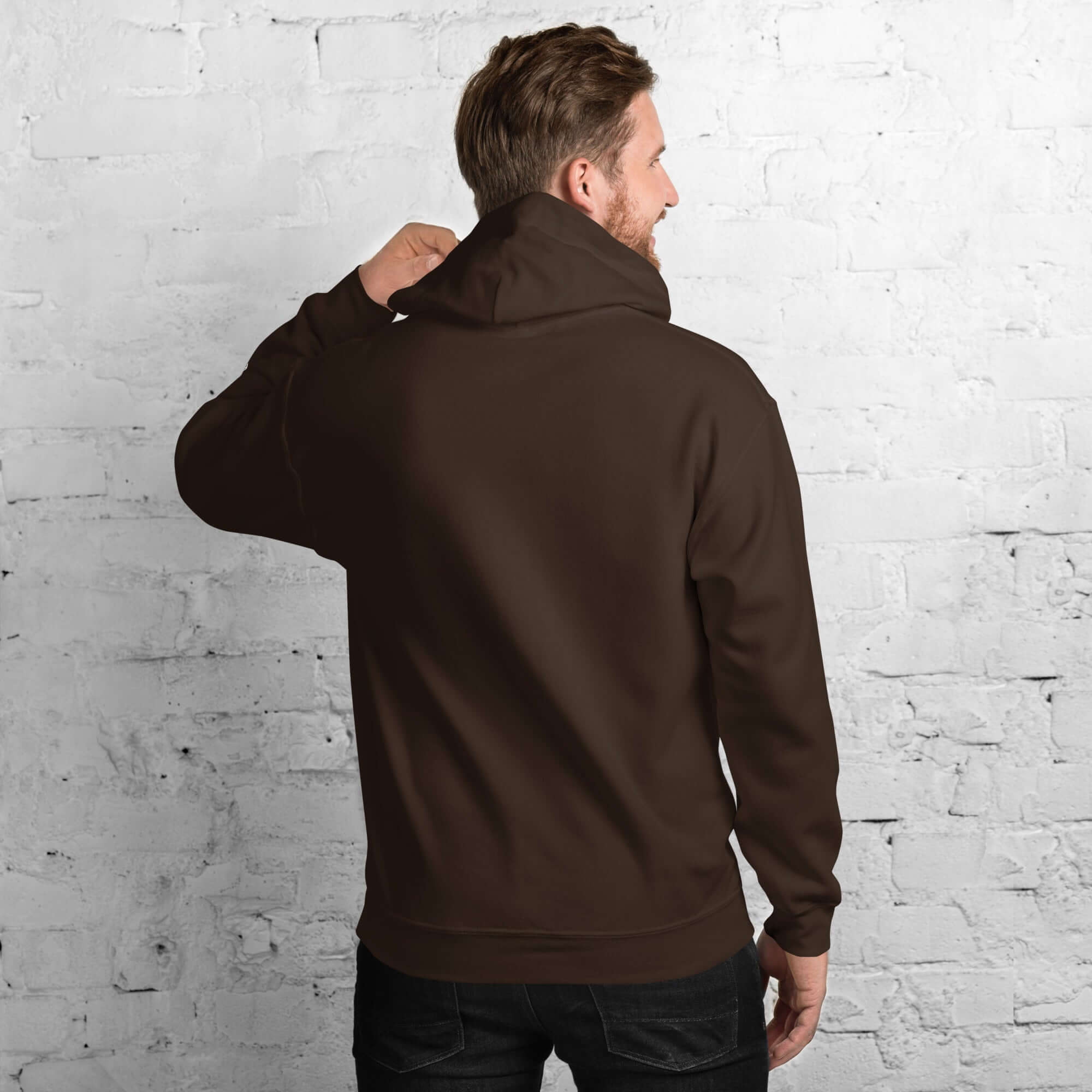 Back view of a man wearing a brown men's hoodie from the Core Collection against a white brick wall.