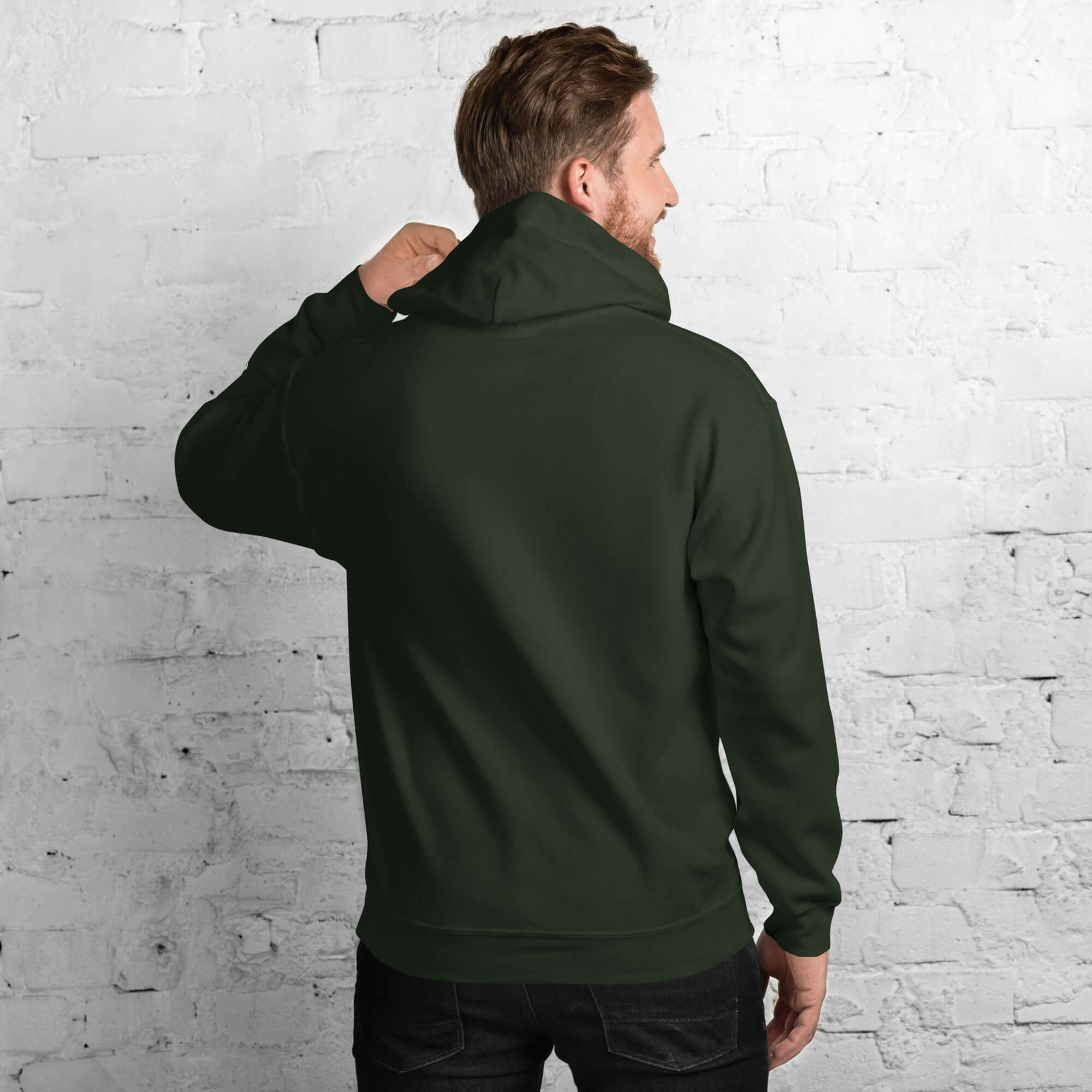 Back view of a man wearing a dark green men's hoodie from the Core Collection against a brick wall.
