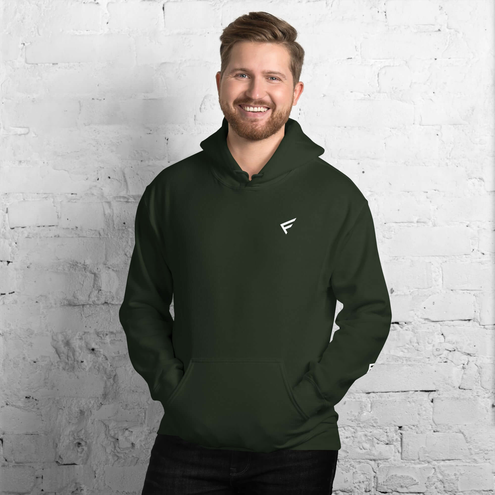 Man wearing a Men's Hoodie from the Core Collection in classic dark green against a brick wall background.