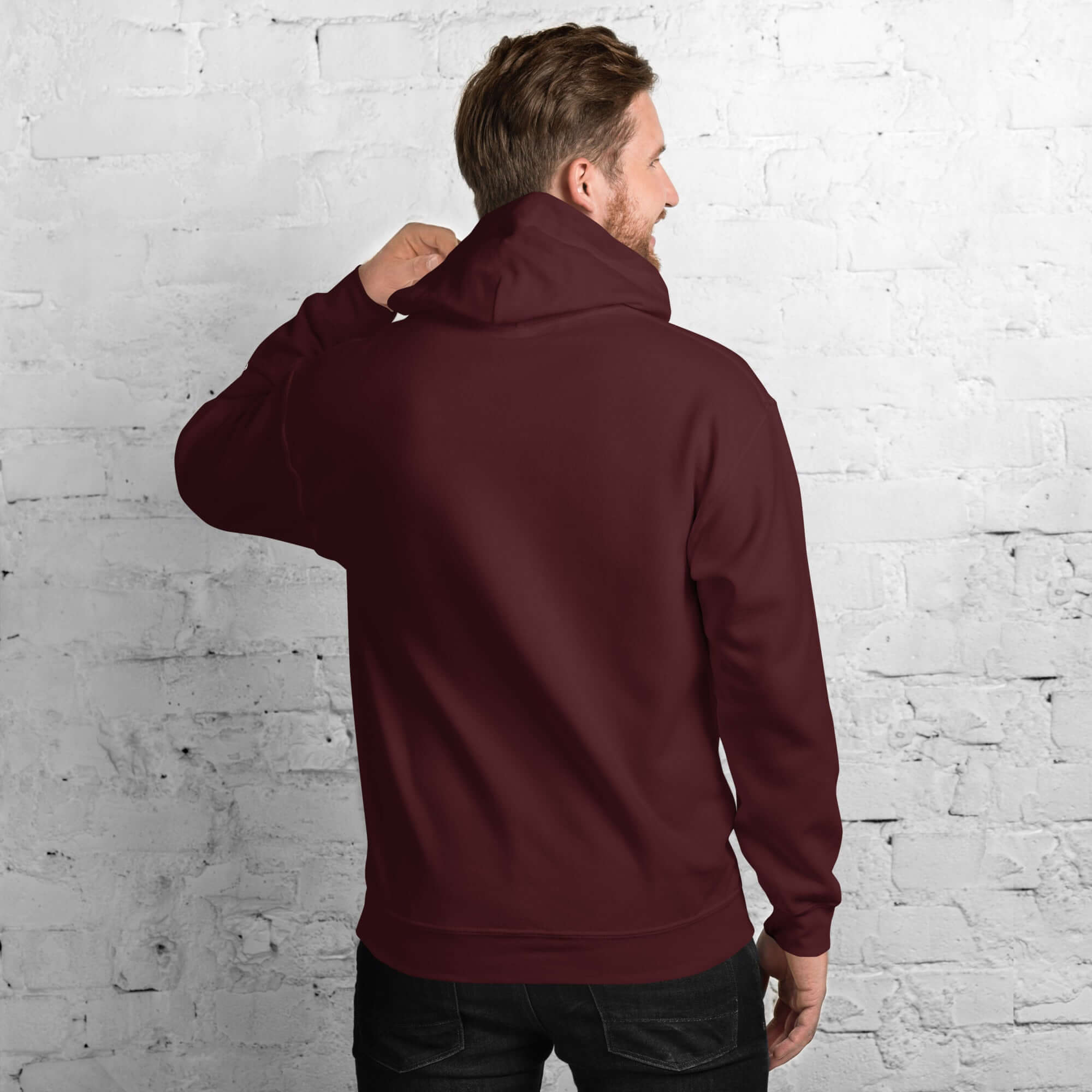 Back view of a man wearing a burgundy men's hoodie from the Core Collection against a textured white brick wall.