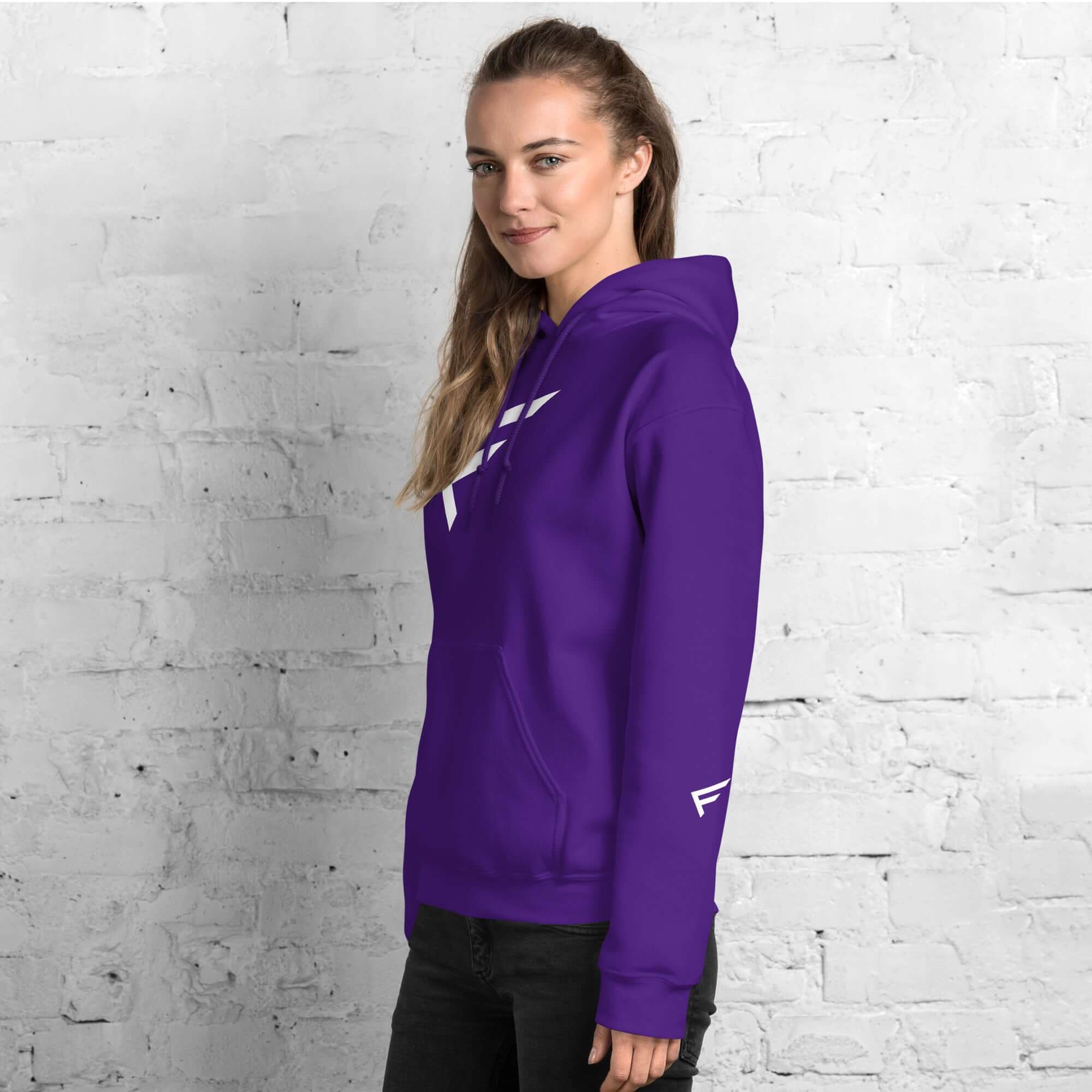 Woman wearing a purple hoodie with the signature 'F' emblem, showcasing comfort and style against a brick wall.